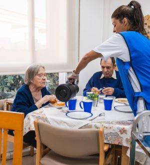 Nurse in blue uniform serving breakfast to elderly residents at a nursing home, fostering a warm and caring environment for seniors